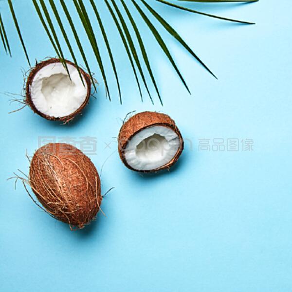 整個和一半的椰子,在藍(lán)色背景上的棕櫚葉和文本空間的副本。一個奇異的水果。扁平放。一個椰子和棕櫚綠葉在藍(lán)色背景上的副本空間。熱帶堅果。扁平放。